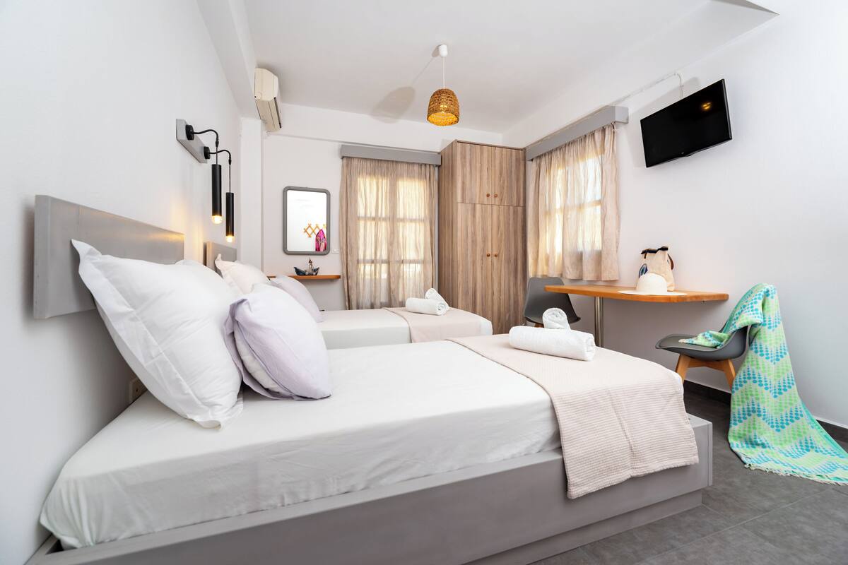 Une chambre d’hôtel moderne équipée de deux lits, d’une télévision, d’un bureau et d’une fenêtre avec des rideaux.