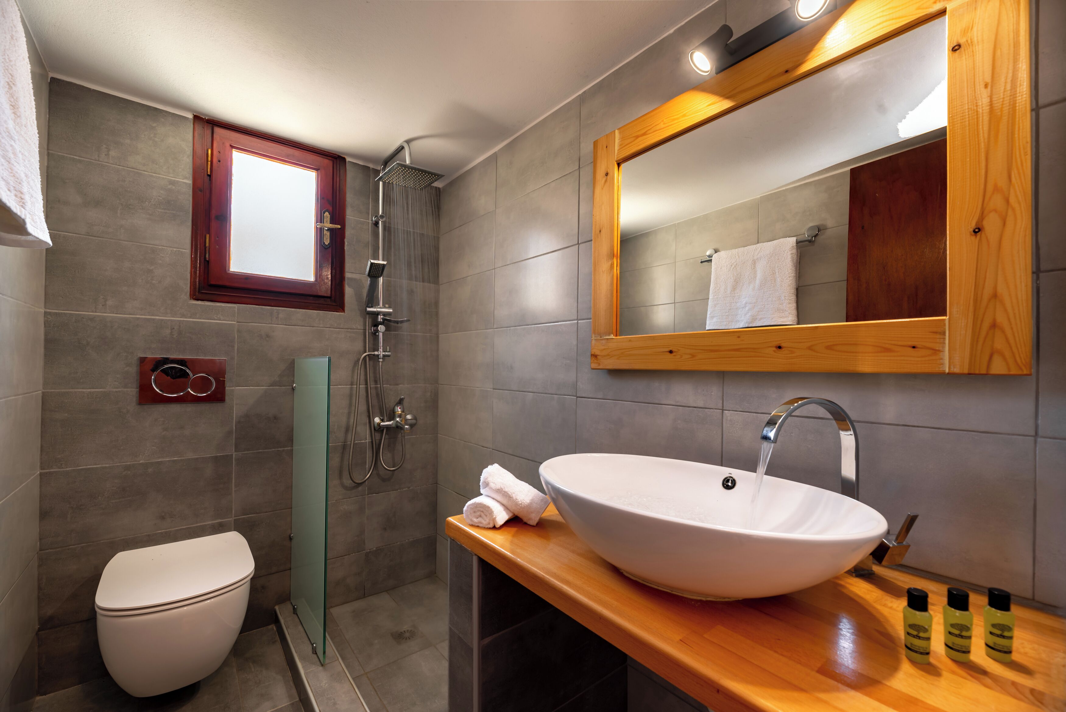 A modern bathroom with a white sink, wooden countertop, and a large mirror.