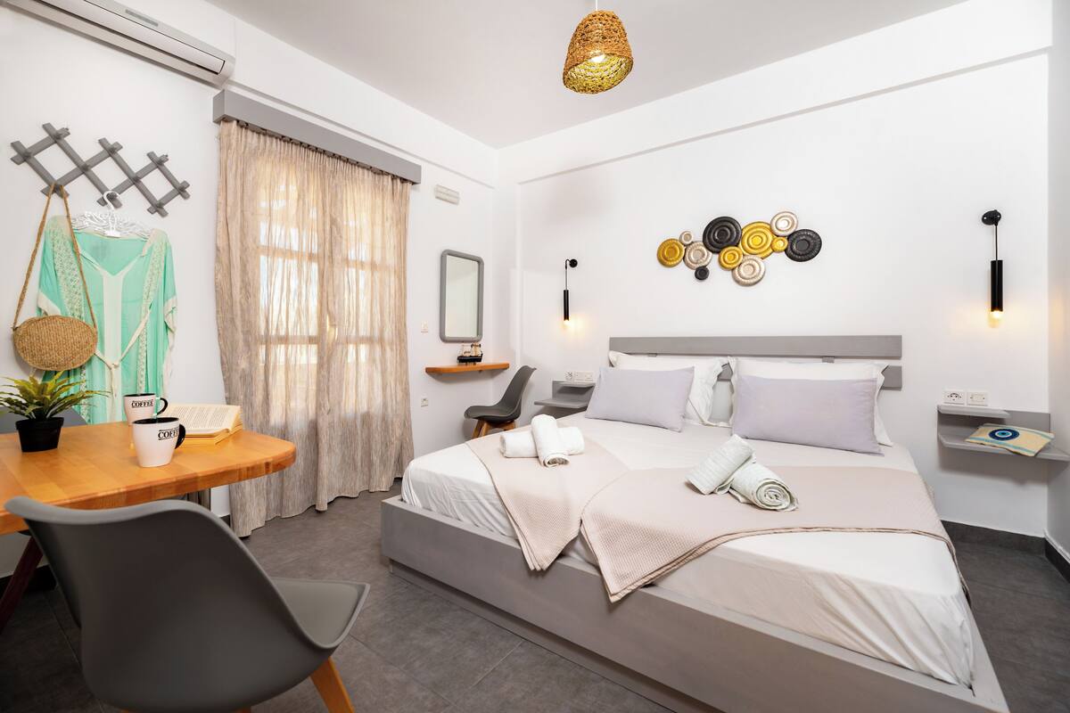 Une chambre d’hôtel moderne équipée d’un lit, d’un bureau avec une tasse à café, d’une chaise, d’un panier suspendu et d’un miroir fixé au mur.