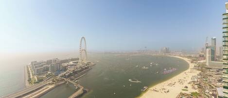 An aerial view of a coastal city with a prominent Ferris wheel, a beach, and modern high-rise buildings.
