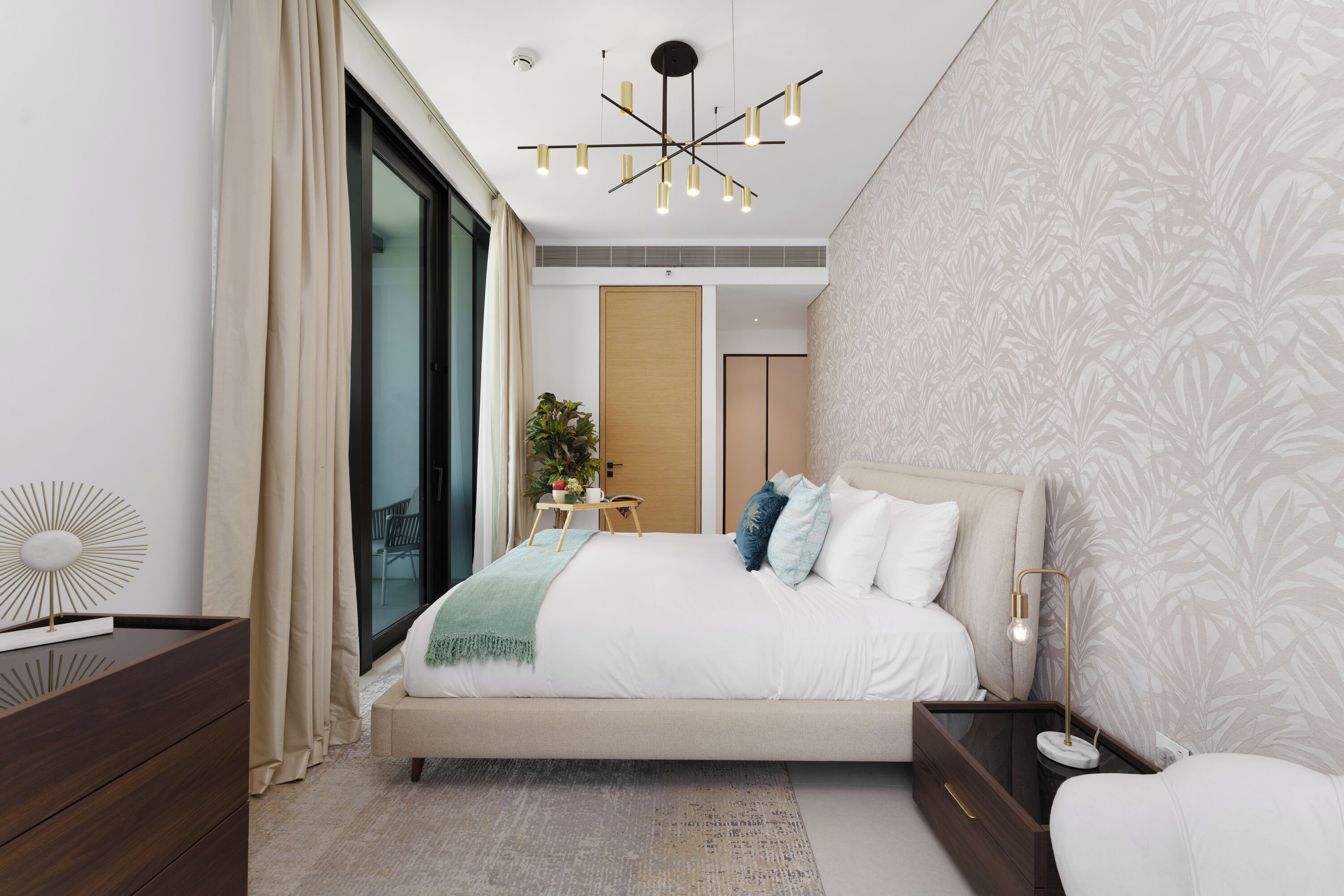 A modern bedroom with a large bed, a bedside table, a floor lamp, and a view of the outdoors through a sliding door.