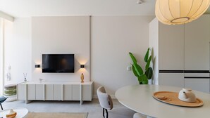 A modern living room with a flat-screen TV, a dining table with chairs, a large potted plant, and a pendant light. - Zoutelande Retreat by Sea (Zoutelande)