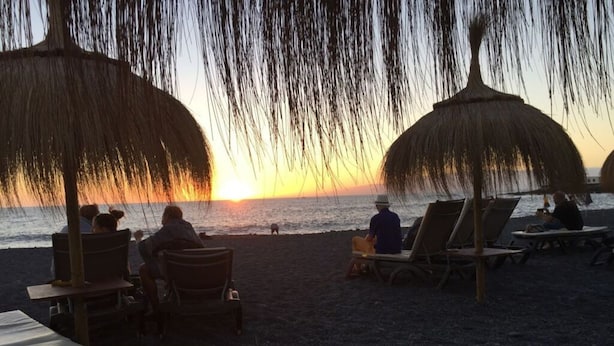 A beach scene with thatched umbrellas, lounge chairs, and a sunset view. - Apartment The Little La Perla (Arona)