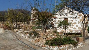 A stone building with a rustic exterior, a small porch, and a garden area with plants and a bench. - Apartment The Little La Perla (Arona)