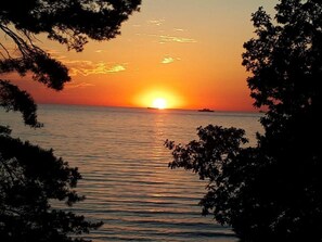 Ein Sonnenuntergang über einem ruhigen Meer, mit Baumgruppen, die den Blick einfassen.