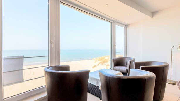 A modern living room with large windows, a view of the beach, and dark leather furniture. - Koksijde Beachfront Vitalo 502 (Koksijde)