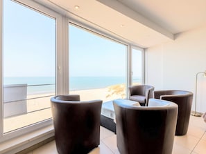 Un salon moderne doté de grandes fenêtres, offrant une vue sur la plage, et meublé de pièces en cuir foncé.