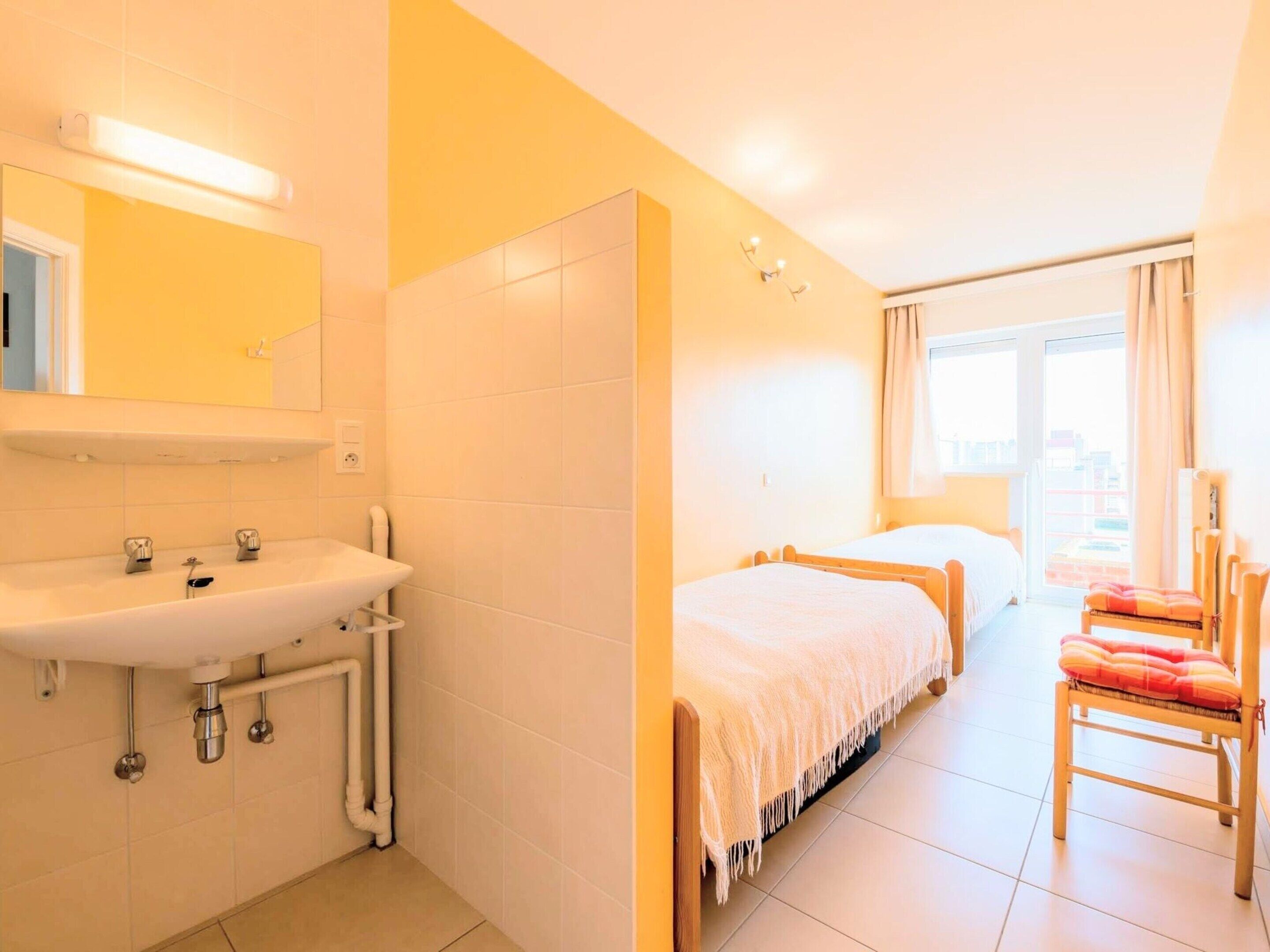 A hotel room with a bathroom, two beds, a chair, and a window.