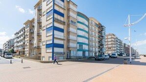 A multi-story residential building with balconies, a paved pedestrian area, and parked cars. - Koksijde Beachfront Vitalo 502 (Koksijde)