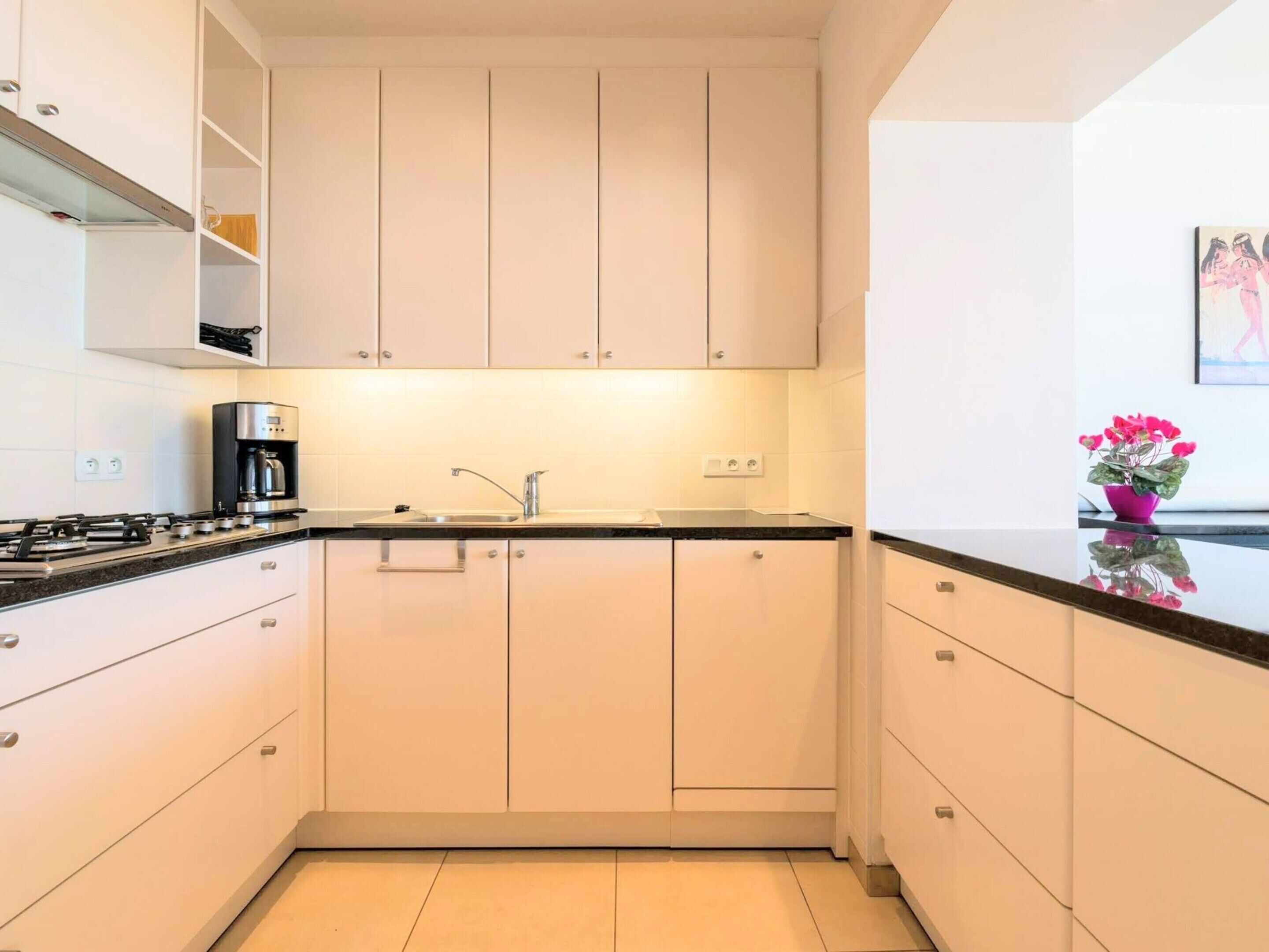 A modern kitchen with white cabinets, a black countertop, and a gas stove.