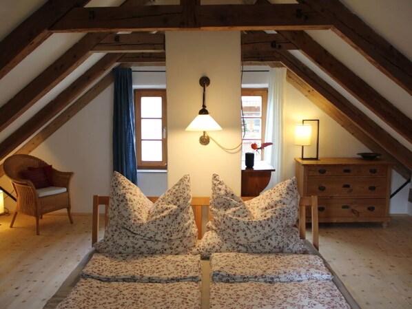 Un dormitorio acogedor en el ático con techo de madera, cama con ropa de cama floral, una silla, un aparador y una lámpara.