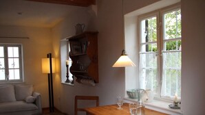 Une pièce chaleureuse avec une table en bois, des chaises, une lampe, une bibliothèque et une fenêtre donnant sur un paysage verdoyant.