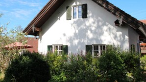 Une maison blanche avec des volets verts, un toit en pente et un jardin à l’avant.