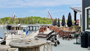 A waterfront patio with wooden tables and chairs, a boat docked at the pier, and a crane in the background. - 4 Star Holiday Home in Grisslehamn (Grisslehamn)