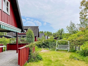 A red building with a deck, a green metal swing set, and a grassy yard. - 4 Star Holiday Home in Grisslehamn (Grisslehamn)