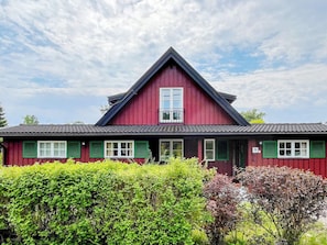 A red building with a gabled roof and green shutters, surrounded by greenery. - 4 Star Holiday Home in Grisslehamn (Grisslehamn)