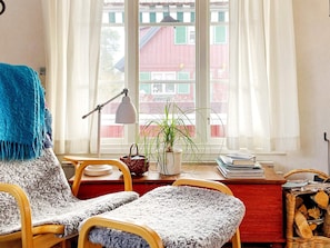 A cozy room with a wooden desk, a chair, a lamp, a potted plant, and a view of a red building through a window. - 4 Star Holiday Home in Grisslehamn (Grisslehamn)