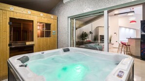 A hot tub in a room with wooden walls and a glass door leading to a kitchen area. - Istra Kamen Comfortable Holiday Residence (Liznjan)