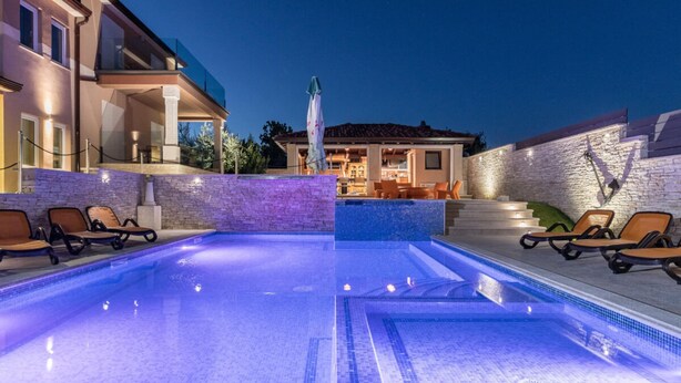 A pool area with lounge chairs, a stone wall, and a building with a tiled roof in the background. - Istra Kamen Comfortable Holiday Residence (Liznjan)