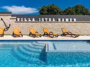 Ein Schwimmbecken mit Liegestühlen und einer Steinmauer mit dem Schriftzug 'VILLA ISTRA KAMEN'.