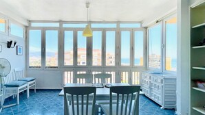 A bright room with a large window, a table, chairs, and a fan.