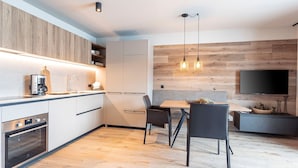 A modern kitchen with built-in appliances, a dining area with a table and chairs, and a flat-screen TV mounted on the wall. - Luxury Apartment, Alpenrosenbahn Within Walking Distance (Westendorf)