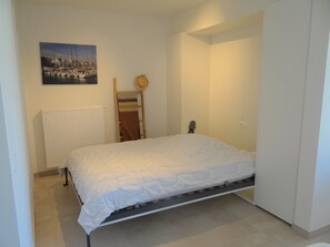 A bedroom with a bed, a radiator, a wooden ladder, a towel, and a painting on the wall. - Nieuwpoort Beach Getaway (Koksijde)