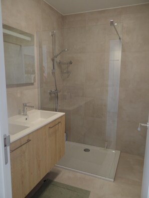 A modern bathroom with a glass shower enclosure, a sink with a mirror, and wooden cabinets. - Nieuwpoort Beach Getaway (Koksijde)