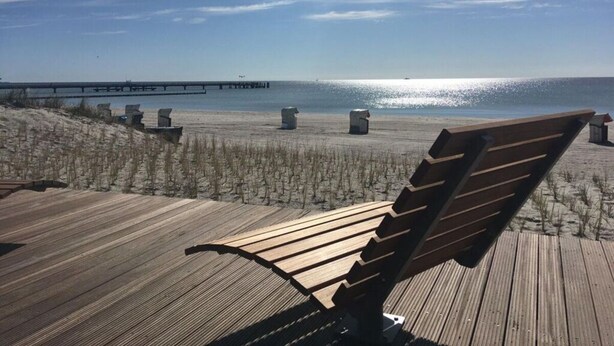 Un banco de madera con vistas a una playa y un muelle a lo lejos.