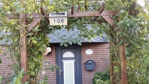 Una casa de ladrillo con una puerta azul oscuro, una pérgola de madera con el número 106 y un buzón en la pared.