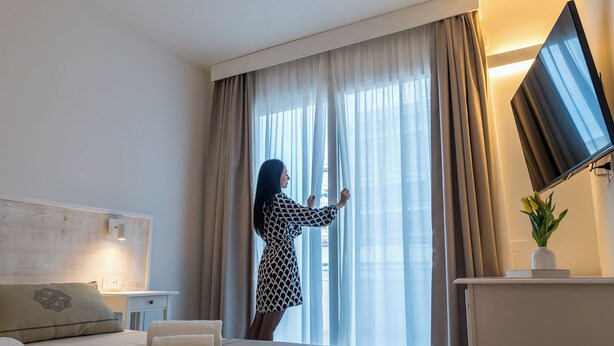 Habitación de hotel con cama, escritorio, televisor de pantalla plana y ventana con cortinas.