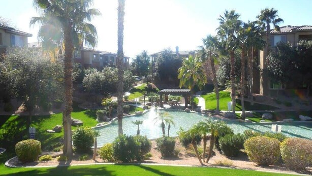 Una piscina rodeada de palmeras y céspedes cuidados, con edificios al fondo.