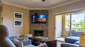 Una sala de estar con chimenea de piedra, un televisor de pantalla plana montado encima y un ventanal corredero que da a un patio exterior.