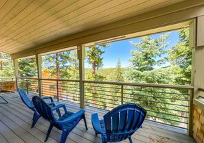 Une terrasse couverte avec trois chaises Adirondack bleues, un plafond en bois et une vue sur les arbres et les bâtiments.