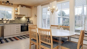 A modern kitchen with wooden cabinets, a stainless steel dishwasher, and a dining area with a round table and wooden chairs. - 5 Person Holiday Home in Laeso (Læsø)