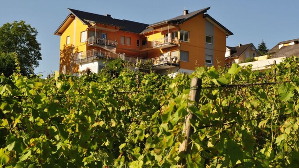A two-story house with a balcony on the upper floor, surrounded by lush greenery. - Sonnenhof Holiday Apartment 4 (Enkirch)