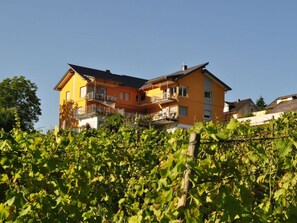 A two-story house with a balcony on the upper floor, surrounded by lush greenery. - Sonnenhof Holiday Apartment 4 (Enkirch)