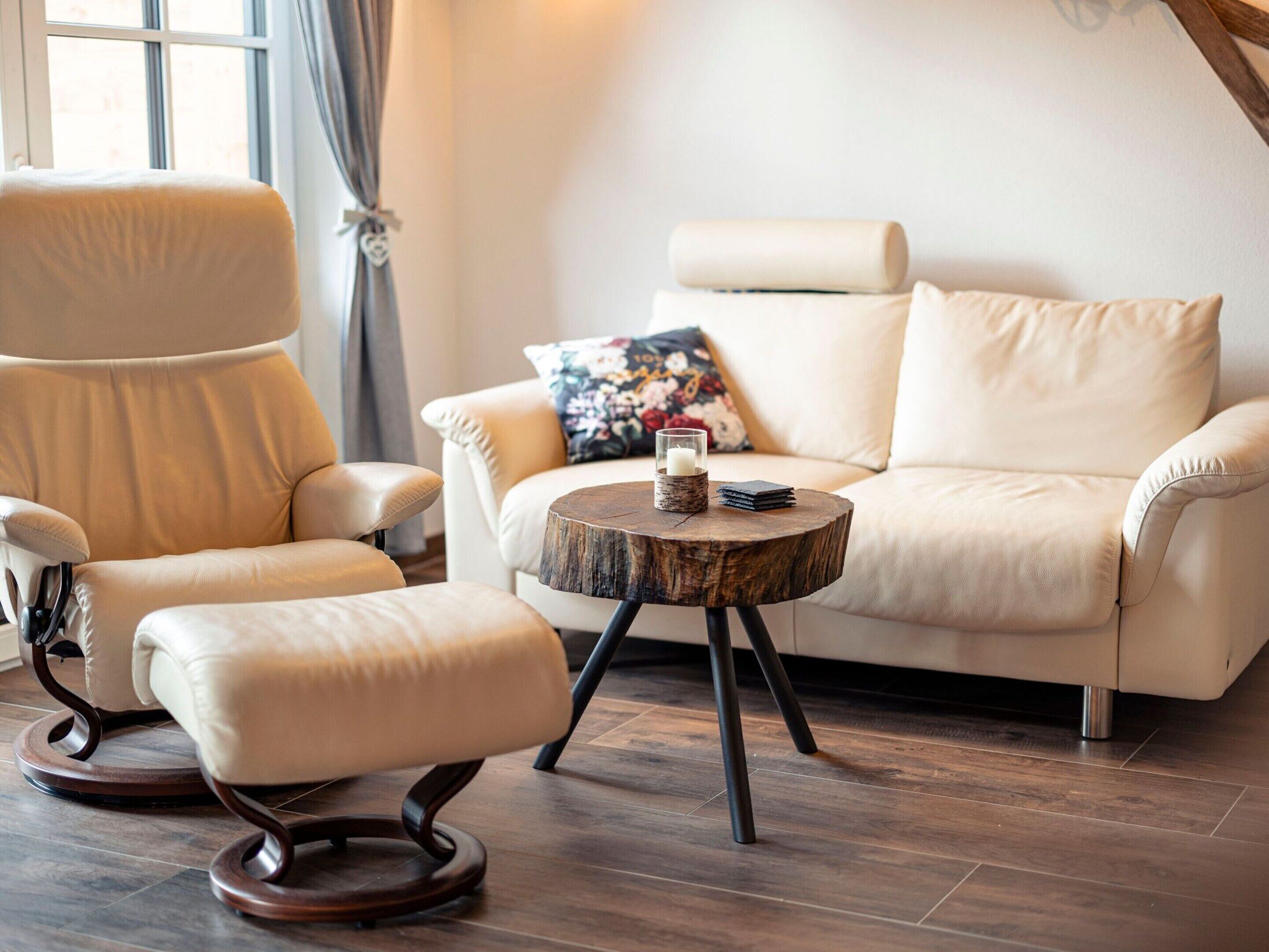 A modern living room with a leather armchair, a sofa, and a round wooden coffee table with a candle and a book.