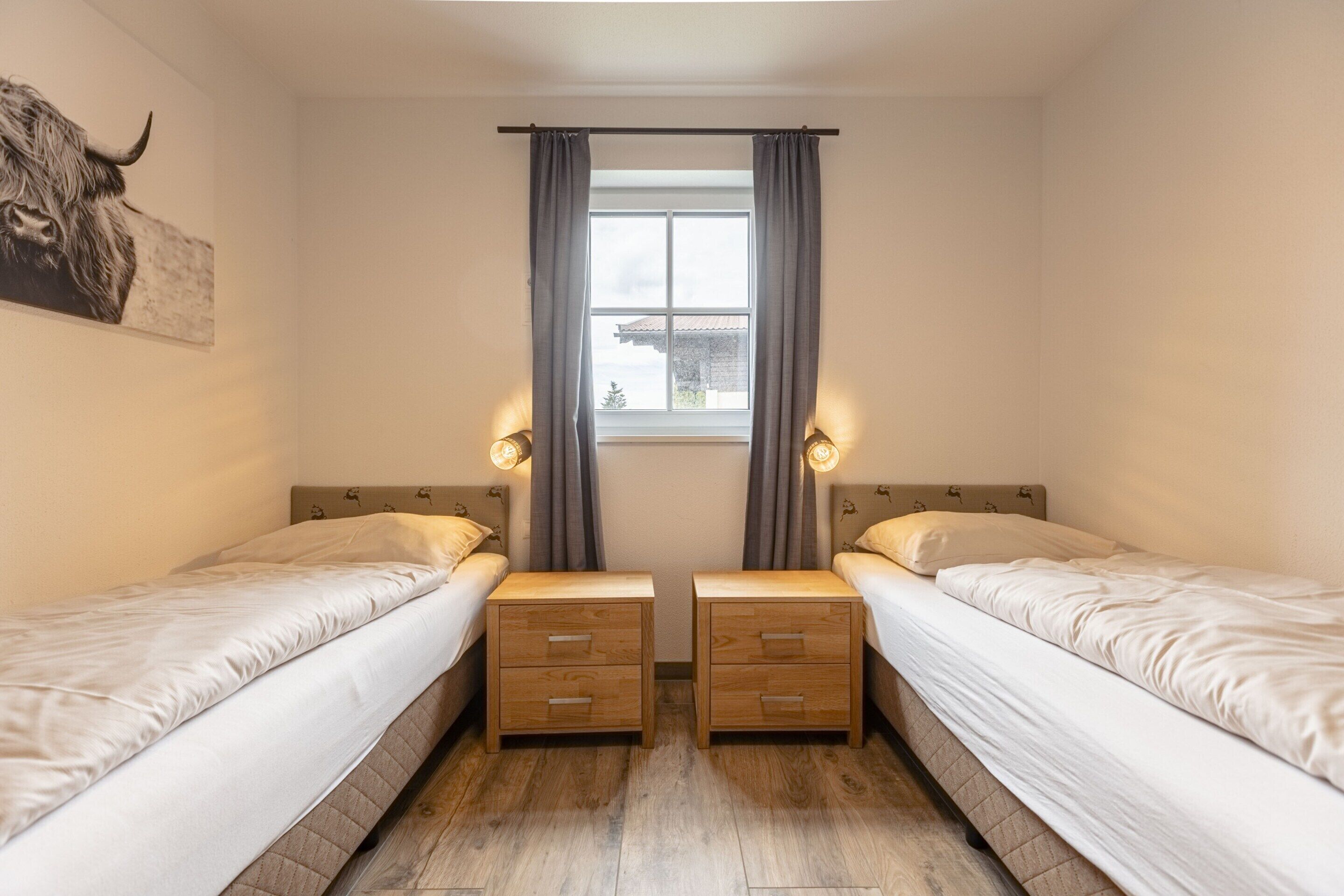 A twin room with two single beds, a window with curtains, bedside lamps, and a bull painting on the wall.