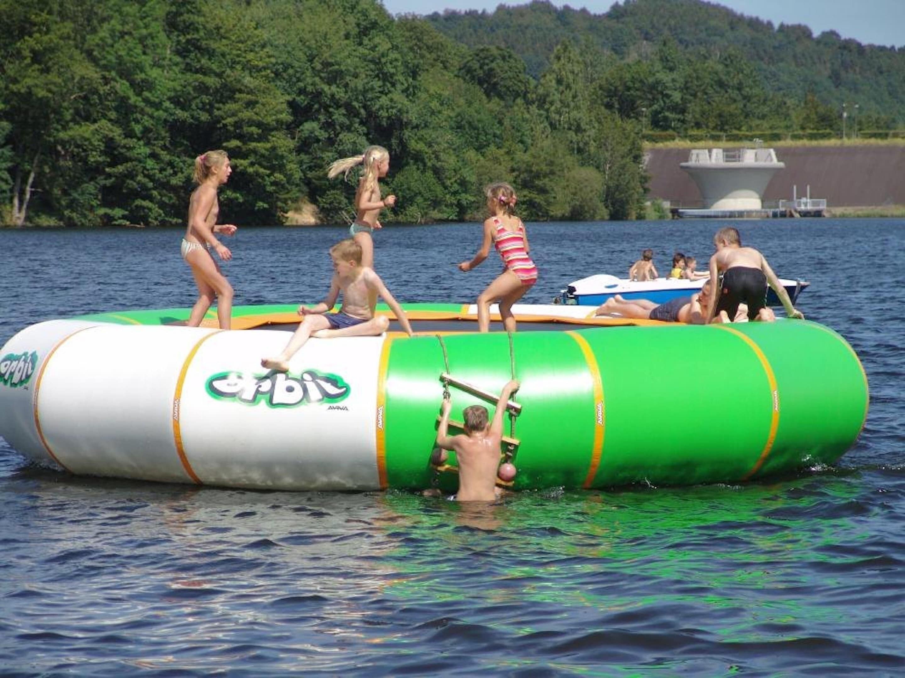 Un gruppo di persone su un'imbarcazione gonfiabile verde e bianca su un lago, con alberi sullo sfondo.