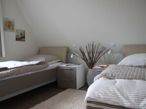 A bedroom with two beds, a bedside table with a lamp, a small plant, and artwork on the wall. - Rieten Huis "oostzeegolf" (Boltenhagen)