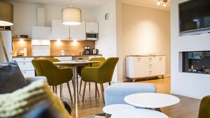 Un salon moderne avec un canapé, une table basse et un coin repas avec des chaises. On aperçoit au fond une cuisine équipée de meubles et d’appareils électroménagers.