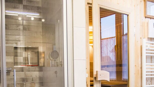 Une salle de bain moderne dotée d’une douche à parois de verre, d’une porte en bois donnant accès à un espace de rangement et d’un porte-serviettes visible.