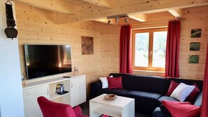 Ein gemütliches Blockhaus mit Holzeinrichtung, einem großen Fernseher, einer Couch und einem roten Sessel.