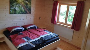 Ein Schlafzimmer einer Holzhütte mit einem Bett, einem Fenster mit roten Vorhängen und einem Bild an der Wand.