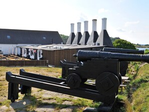 A cannon with a wooden carriage, a building with multiple chimneys, and outdoor seating with umbrellas. - 10 Person Holiday Home in Svaneke (Svaneke)