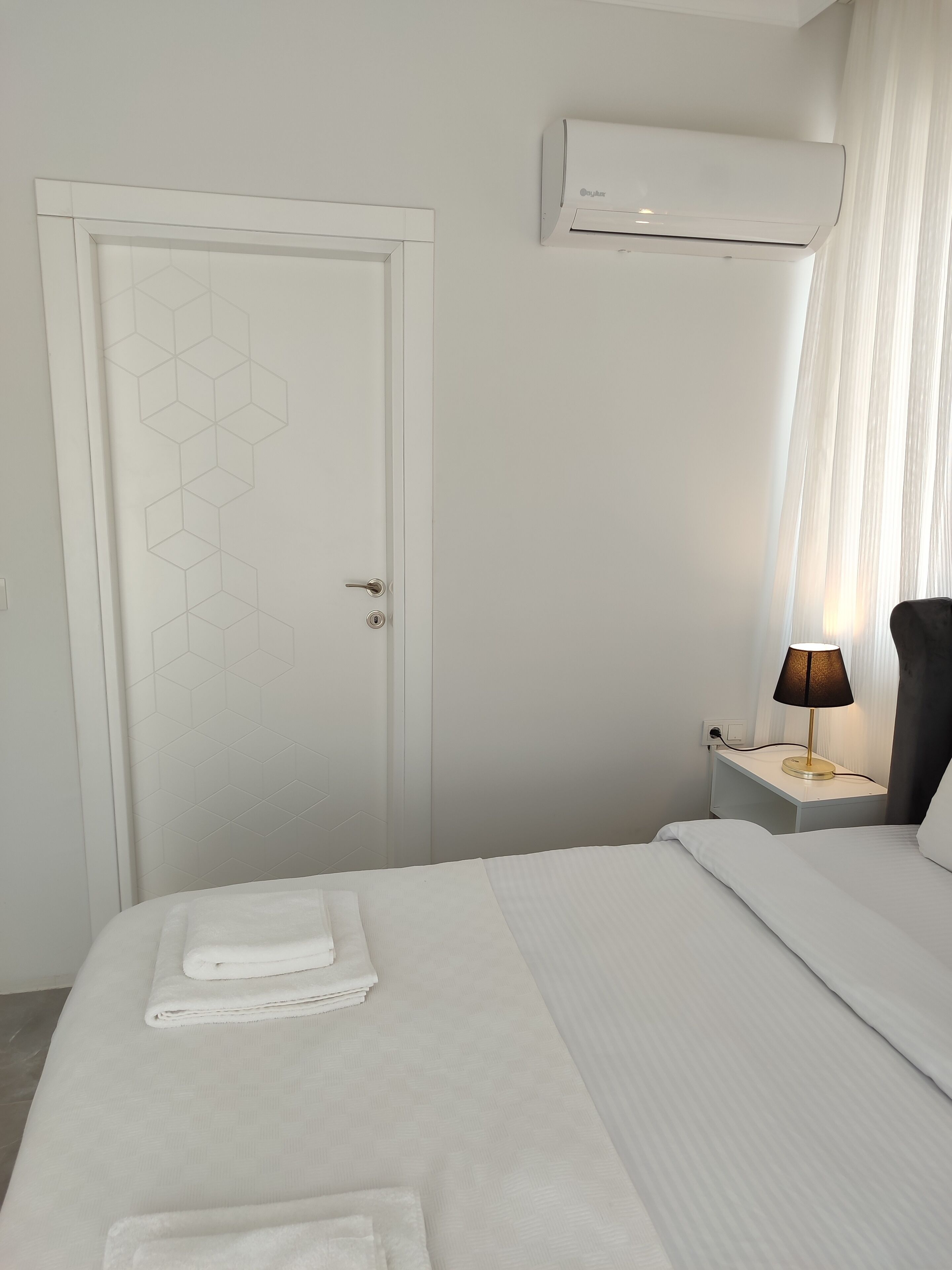 Habitación de hotel con cama, mesita de noche con lámpara, equipo de aire acondicionado y puerta con diseño geométrico.