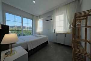 Habitación de hotel con cama, mesita de noche con lámpara, armario y ventana con vistas al exterior.