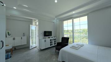 Habitación de hotel con cama, televisión, sillón, escritorio y balcón con vistas.