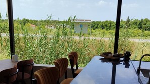 A dining area with a long table and chairs, a water dispenser, and a view of a road and greenery. - The Dalaman Suites & Pension Dalaman Airport 10 km (Dalaman)